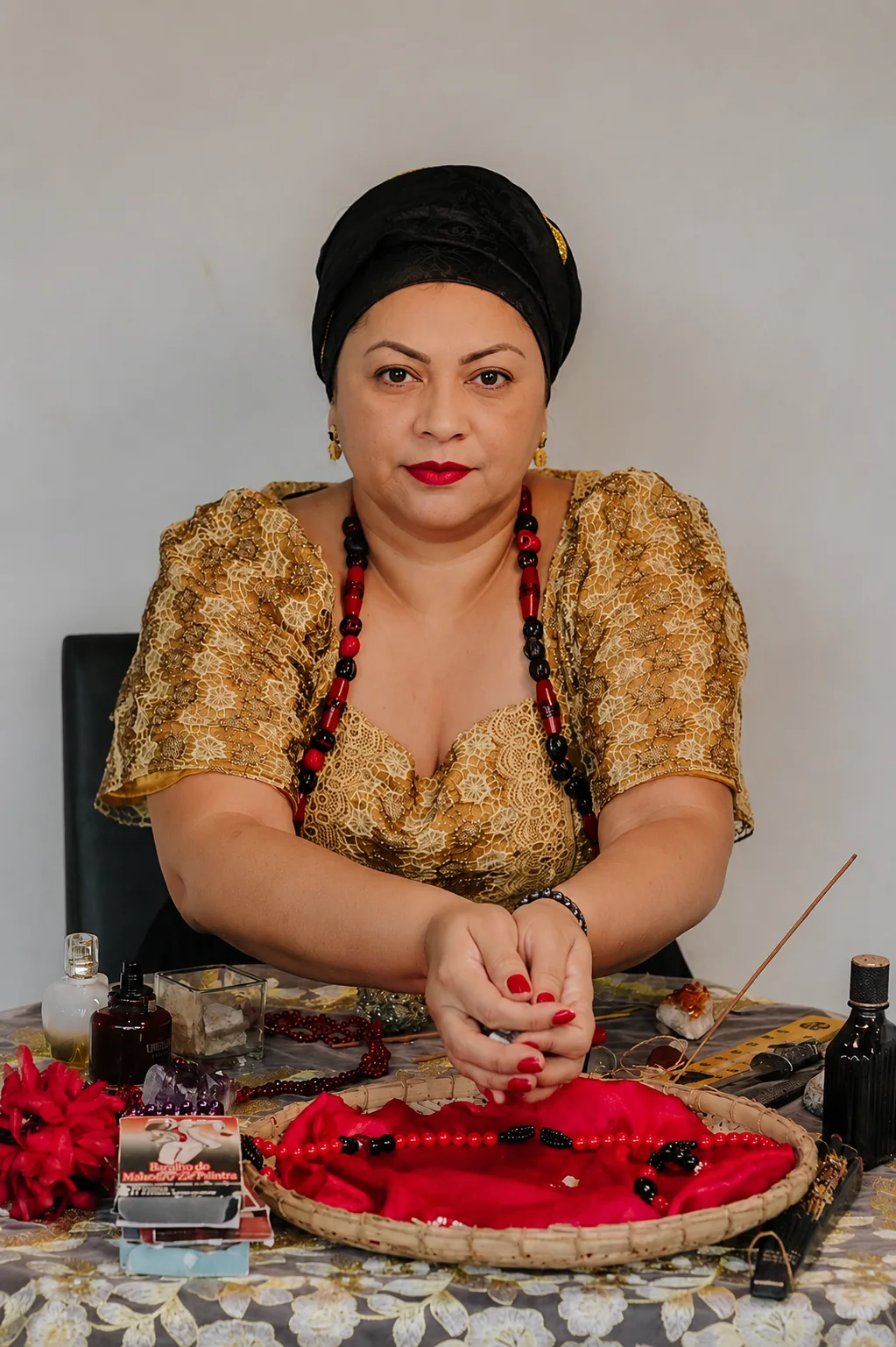 Mãe Lisandra com vestido de renda dourada e turbante preto, em ritual à mesa com bandeja vermelha, cristais, incenso e baralho Zé Pelintra
